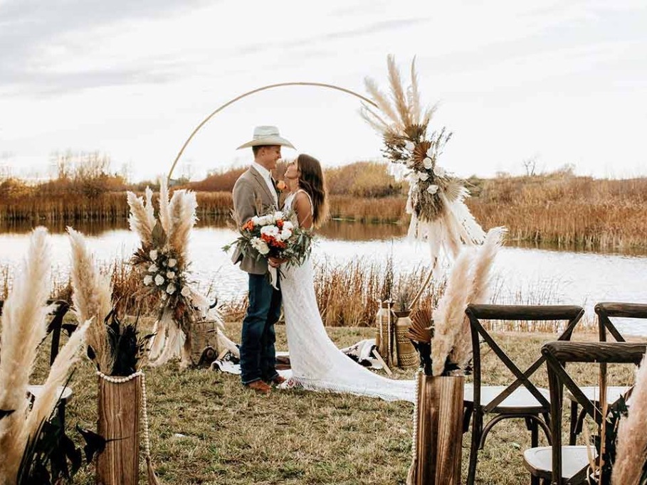 Bride and groom under a floral hoop by the lodge pond