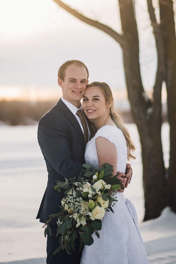 Bride and groom smiling together in the snow beside a tree